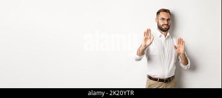 Displeased man rejecting something disturbing, showing stop sign and declining, cringe from aversion, standing over white background Stock Photo