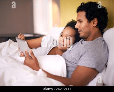 Snuggling while watching our favorite movie. a young couple using a digital tablet while cuddling in bed. Stock Photo