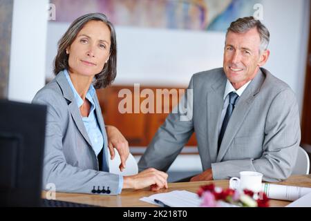 They make a great business team. Portrait of two mature business colleagues sitting beside each other at a desk. Stock Photo