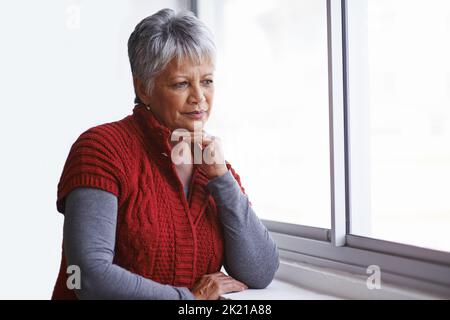 Something on her mind. a mature woman standing by a window on a sunny day. Stock Photo