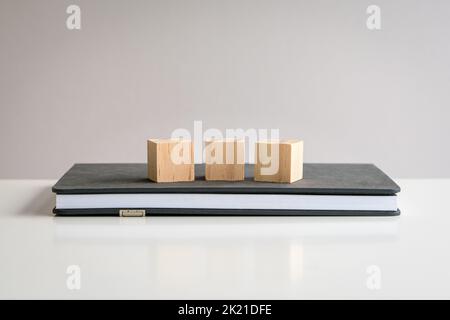 Three blank wooden block cubes on top of a notepad. Free text and template for business concept. Stock Photo