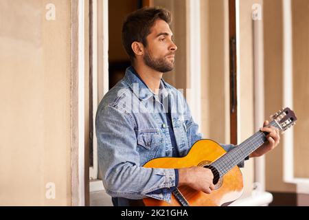 Do more of what makes you happy. a handsome young man relaxing on the patio while playing a guitar. Stock Photo