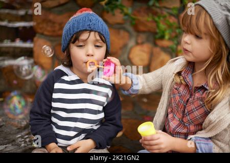 Showing him how its done. two cute kids blowing bubbles together outdoors. Stock Photo