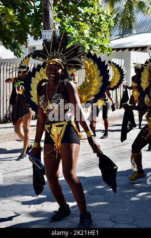 A young Belizean woman smiling at the camera dancing in the San Pedro, Belize, Carnival 2022. She is wearing a winged, shiny, black and gold costume. Stock Photo
