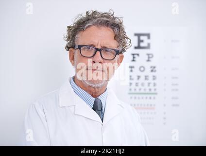 Trust him to take care of your eyes. Portrait of a mature optometrist standing in front of an eye chart. Stock Photo