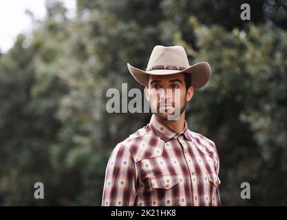 Wild west wrangler. a handsome man wearing a check shirt and cowboy hat. Stock Photo