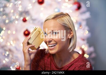 I hope its not breakable. Portrait of a smiling young woman holding a present to her ear. Stock Photo