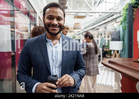 Portrait of indian businessman standing in modern office on colleagues background Stock Photo