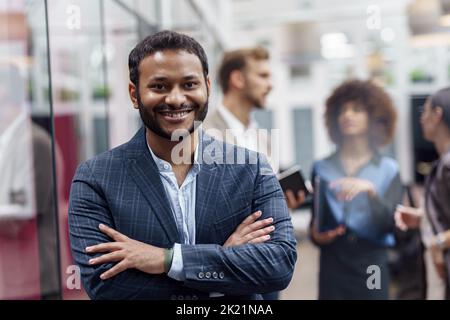 Portrait of indian businessman standing in modern office on colleagues background Stock Photo