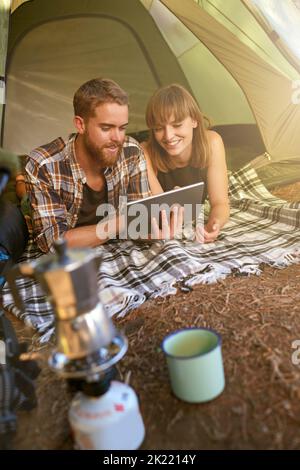 Into the woods. a young couple lying in a tent looking using a digital tablet. Stock Photo