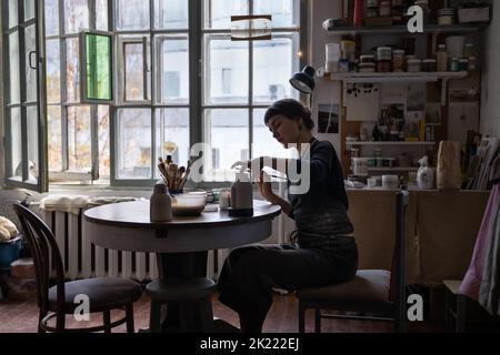 Young skilled lady concentrated on modeling jug from raw clay enjoys hobby creating vase Stock Photo