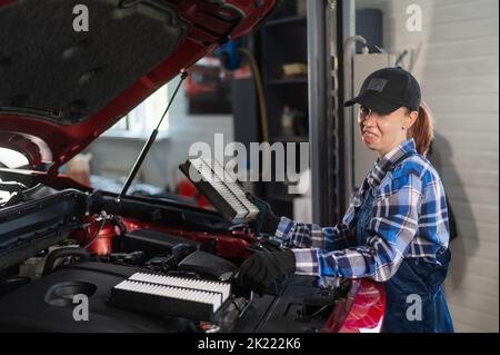 Caucasian female auto mechanic changes the engine air filter in the car. Stock Photo