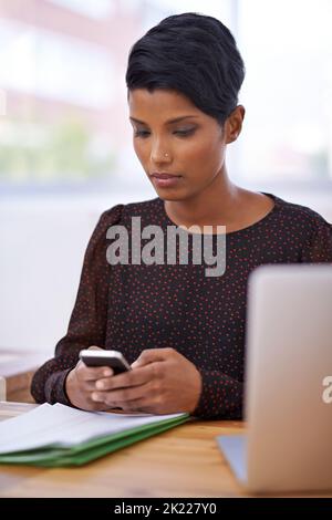 Checking her calendar. A beautiful young woman sending a text message while sitting in her office. Stock Photo