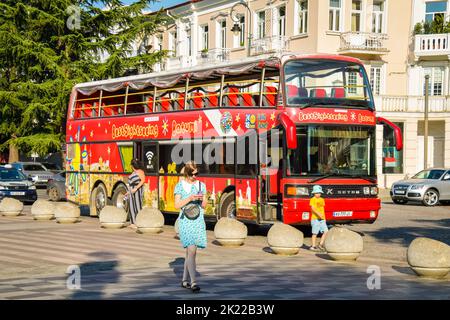 Batumi, Georgia - 4th august, 2022: female tourist walk us phone in street pass red two floor double-decker classic sightseeing bus around city. Famou Stock Photo