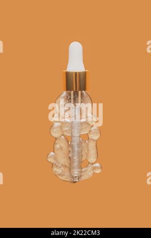 Liquid serum and dropper on an orange peach background, top view. Serum drops in the form of a bottle with a pipette. Stock Photo