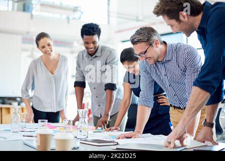 Collaborative brainstorming for powerful strategies. Group of diverse professionals gathered at a table to look at a strategic plan. Stock Photo