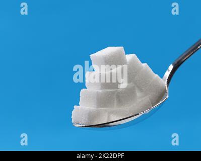 sugar cubes pyramid on silver spoon isolated on blue background with copy space Stock Photo