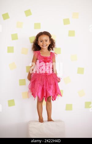 Playing with the sticky stuff. Portrait of a smiling little girl standing in front of a wall full of sticky notes. Stock Photo