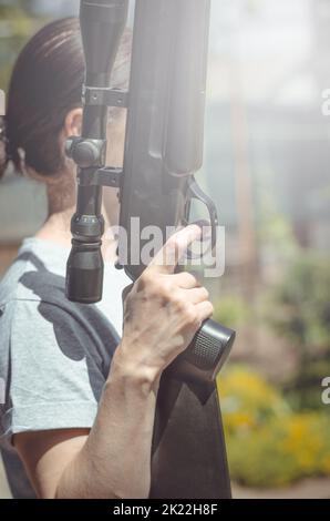 A young woman with a gun in her hands. A woman is holding a large sniper rifle, close-up. Air rifle with optical sight Stock Photo