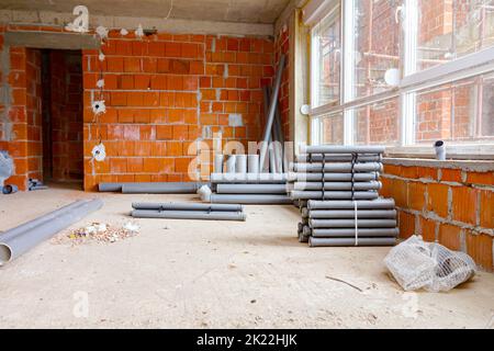 Arranged new grey plumbing sewer pipes are laid down on the floor waiting to be installed, view on scaffolding through the window of building under co Stock Photo