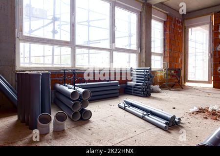 Arranged new grey plumbing sewer pipes are laid down on the floor waiting to be installed, view on scaffolding through the window of building under co Stock Photo