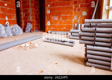 Arranged new grey plumbing sewer pipes are laid down on the floor waiting to be installed into a building under construction. Stock Photo