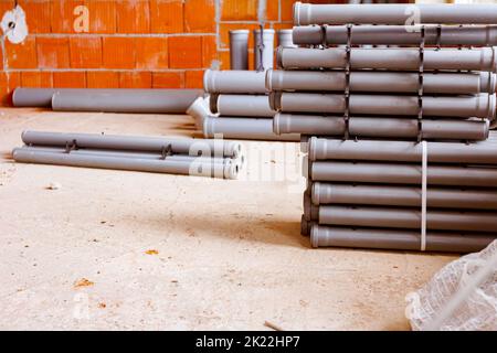 Arranged new grey plumbing sewer pipes are laid down on the floor waiting to be installed into a building under construction. Stock Photo