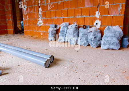 Stack of arranged parts of new grey plumbing sewer pipes elbows placed in mesh sacks waiting to be installed into a building under construction. Stock Photo