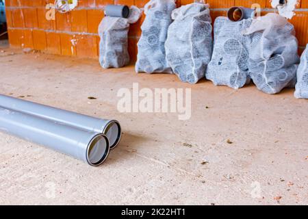 Stack of arranged parts of new grey plumbing sewer pipes elbows placed in mesh sacks waiting to be installed into a building under construction. Stock Photo