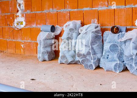 Stack of arranged parts of new grey plumbing sewer pipes elbows placed in mesh sacks waiting to be installed into a building under construction. Stock Photo