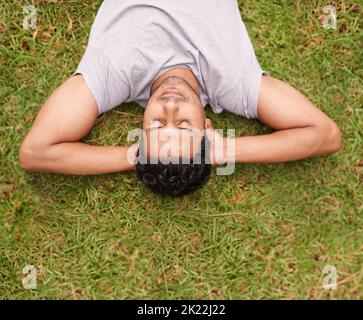Taking time out to relax. A young man lying on the grass with his hands behind his head. Stock Photo