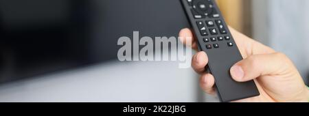 Black remote control in hand in front of TV Stock Photo