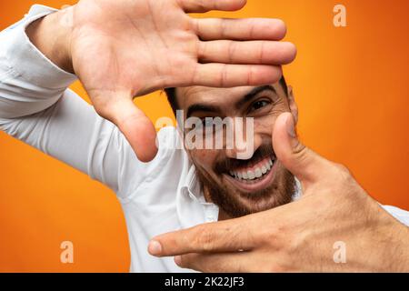 Smiling young man looking at camera and making frame gesture on orange background Stock Photo