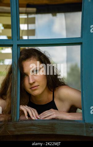 Shot of sad young woman crying while looking through the window at home. Stock Photo
