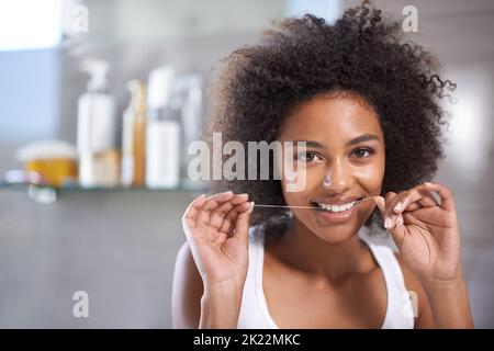 For a bright smile. a young woman flossing her teeth in the mirror. Stock Photo