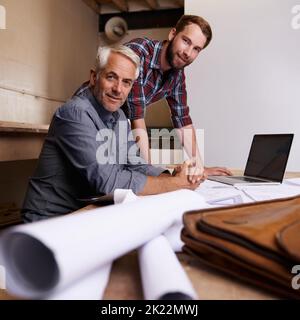 Our project is right on track. Portrait of two architects sitting with a laptop and their building plans. Stock Photo