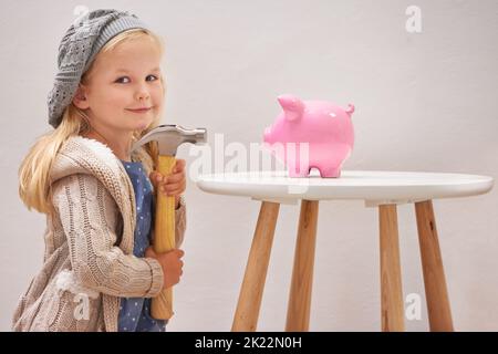 To break or not to break. A little girl standing in front of her piggy bank with a hammer. Stock Photo