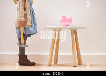 To break of not to break. A little girl standing in front of her piggy bank with a hammer. Stock Photo