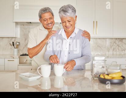 Coffee, couple and love with a senior woman and man enjoying retirement while together in the kitchen of their home. Happy, smile and romance with an Stock Photo