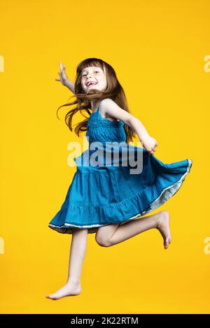 Funny preschooler girl joyfully jumps and smiles. The child is happy. The front milk teeth fell out in the mouth. Isolated on a yellow background. High quality photo Stock Photo