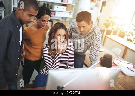Putting their heads together. a group of coworkers gathered around a pc. Stock Photo