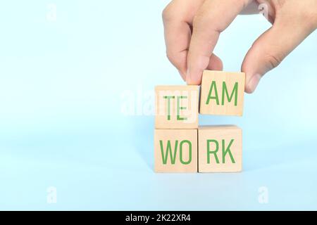 Teamwork and team building business concept. Hand putting together wooden blocks wood puzzle pieces in blue background. Stock Photo