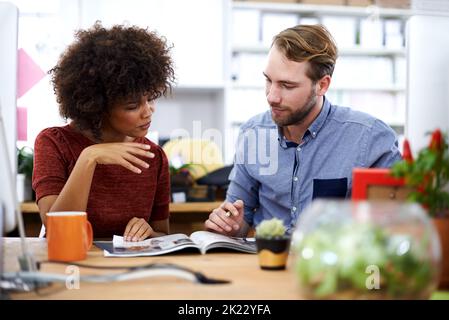 Building on their ideas. two designers having a discussion while paging through a magazine. Stock Photo