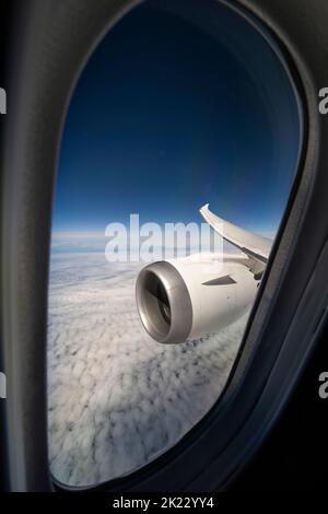 Window view of the right wing and engine of a Boeing B787-1000 Dreamliner flying over the clouds