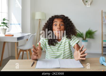 School child sitting at desk and looking at camera with funny, happy, surprised face expression Stock Photo