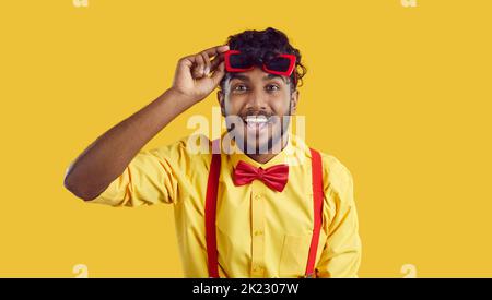 Young cheerful South Asian man raises funny glasses from eyes and looks at screen with smile Stock Photo