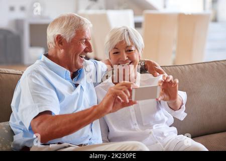 Say cheese to true love. a senior couple taking a selfie with their cellphone while sitting on the sofa. Stock Photo