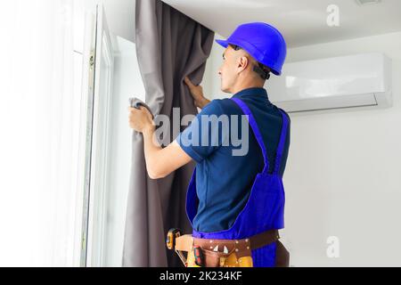 Young handsome man or handyman installing curtains over window at home, doing renovation work. Stock Photo