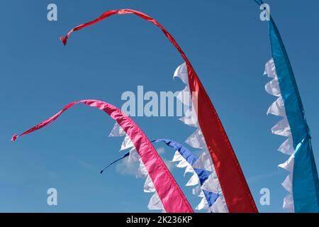 Multi colored flags against a deep blue sky. Red, blue and white pointy banners waving in the wind during a festival. Stock Photo