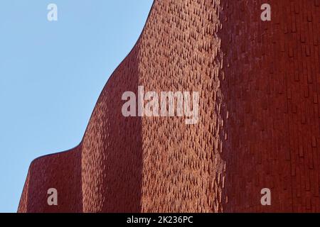 Red brown wavy brick wall of modern architecture with light and shadow under a blue sky in summer. Stock Photo